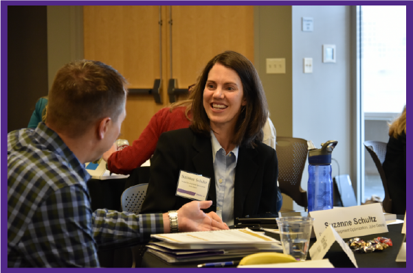 Smiling woman in a blazer talks with a man in a blue plaid shirt at a networking event.